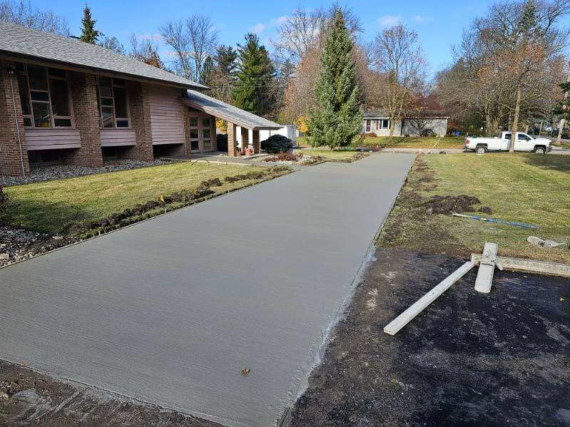 Concrete driveway leading to a brick mid-century home in autumn