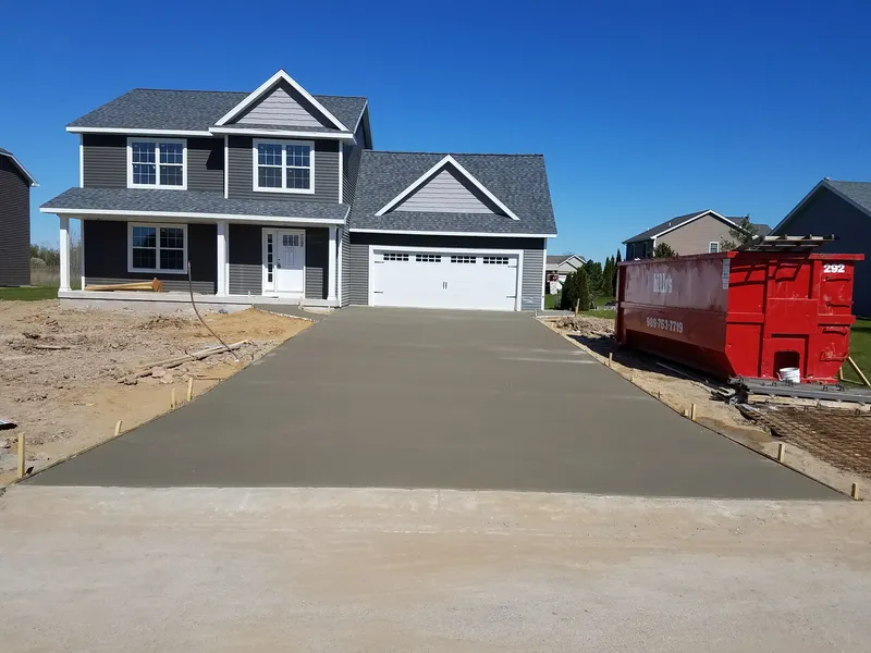 Freshly poured concrete driveway at a new-construction gray two-story home in Mid-Michigan