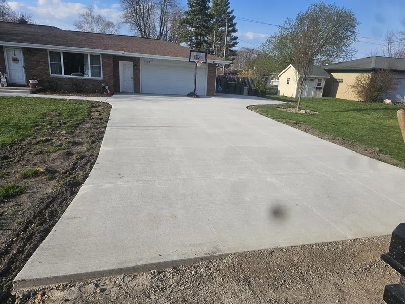 Wide concrete driveway with a basketball hoop at a ranch home